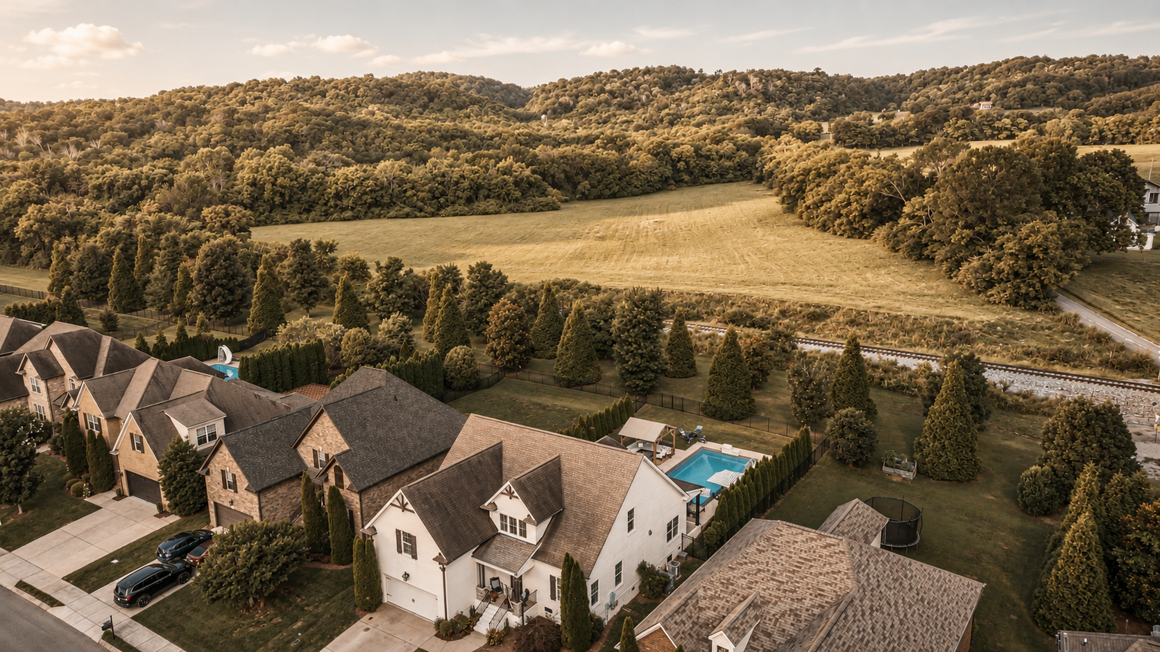 Representative editorial imagery of homes beside open fields and tree-covered hills, not a specific property or neighborhood